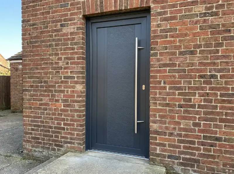 Aluminium voordeur met verticale greep in een bakstenen gevel
